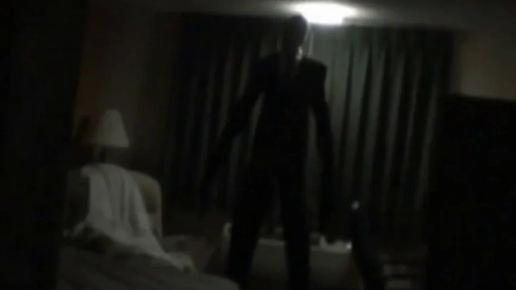 Image tirée de la série Marble Hornet, on y voit le Slender man dans une chambre d'hôtel, tout est sombre et difficile à distinguer.