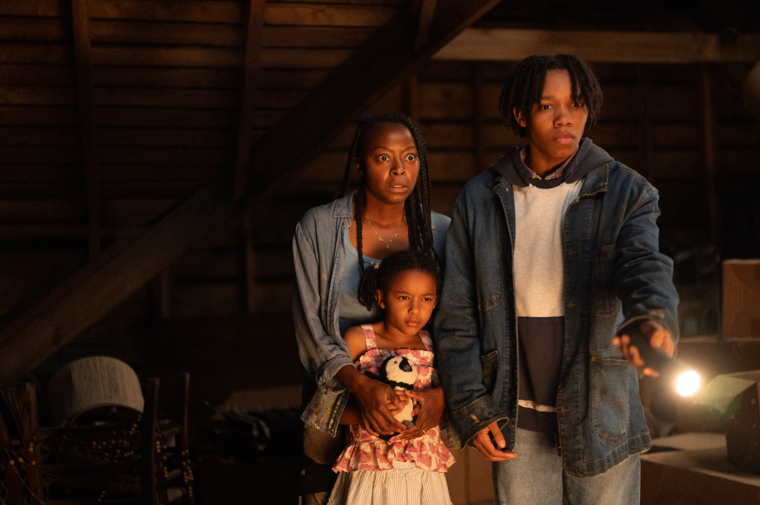 Une famille dans un grenier sombre pointant la torche vers le hors champs, et semblant effrayés.