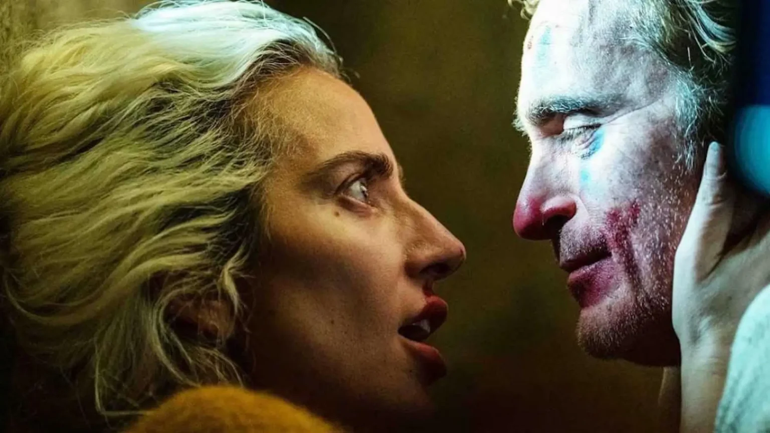 Lady Gagag en Harley Quinn regarde passionnément Joaquin Phoenix en Joker, lui prenant le visage, dans un plan serré.