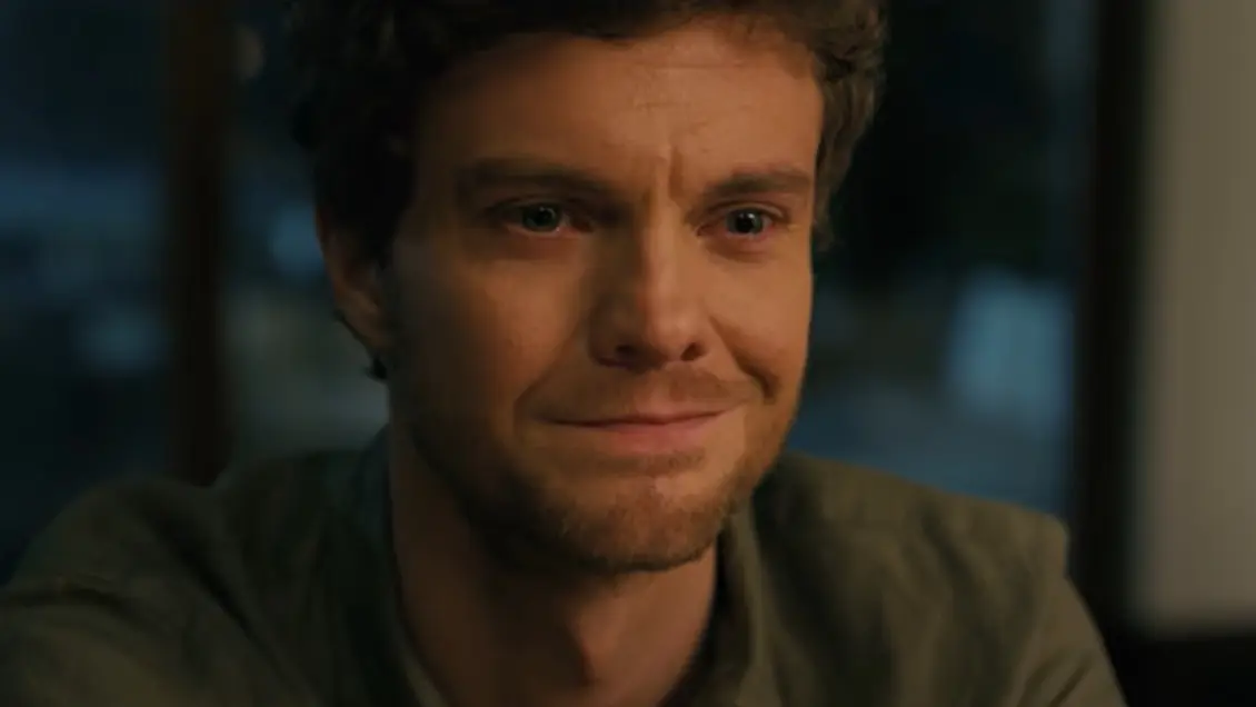 Image tirée du film Companion, un homme en gros plan, les yeux mouillés, ses lèvres forment un sourire à la fois blessée et vindicatif.