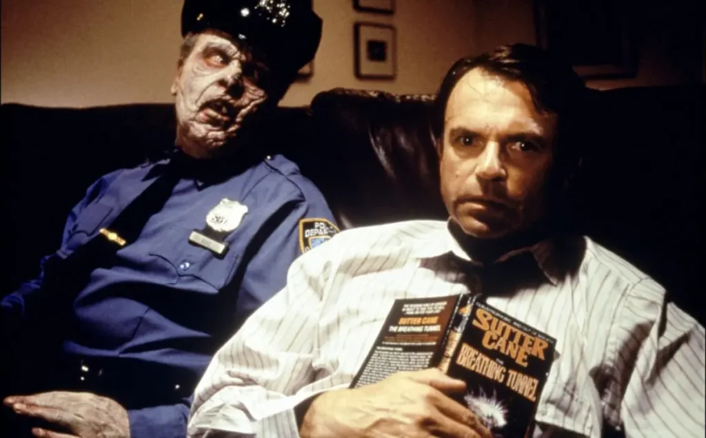 Un homme assis dans un sofa tien un livre ouvert contre lui, son regard est perdu dans le lointain. Il ne semble pas remarquer la présence d'un policier au visage zombifié juste à côté de lui.
