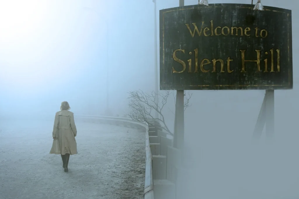 Une femme entre à pied dans une ville complétement recouverte de cendres et de brumes, un panneau sur sa droite indique : Bienvenu à Silent Hill.