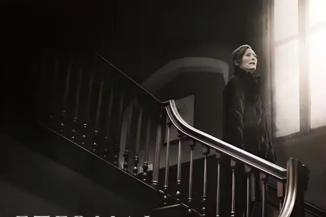 Une femme descend un escalier dans un manoir sombre aux allures spectrales.