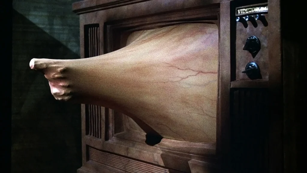 Une main tendant un pistolet sort d'un écran TV. L'écran TV n'est pas en verre mais une membrane organique avec des veine, qui épouse parfaitement la forme de la main qui tente de sortir.