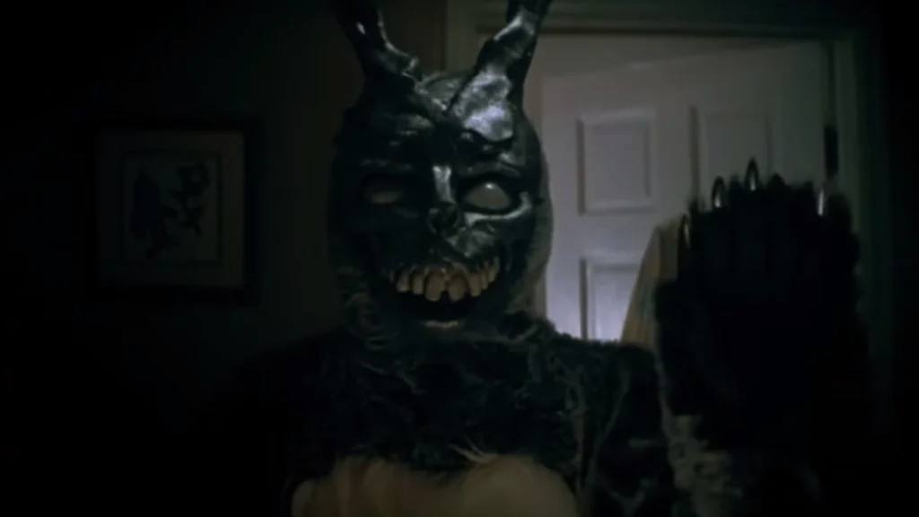 Un homme portant un masque et un costume de lapin dans une chambre la nuit, l'aspect est lugubre. Scène tirée de Donnie Darko.