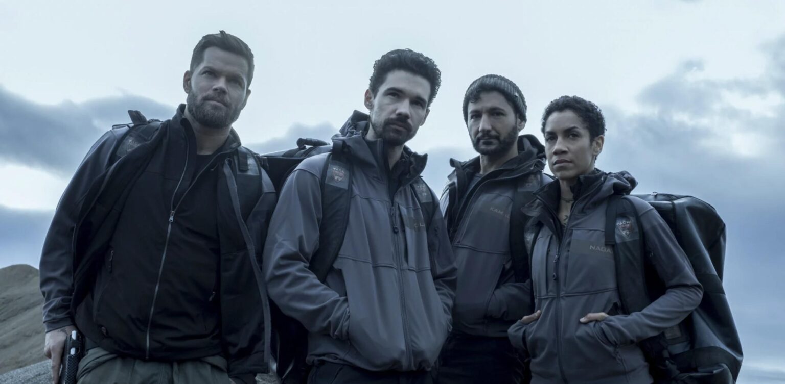 4 personnes, environ la trentaine, regarde dans la même direction, ils sont à l'extérieur et il semble faire froid. l'image est tirée de la série The expanse.