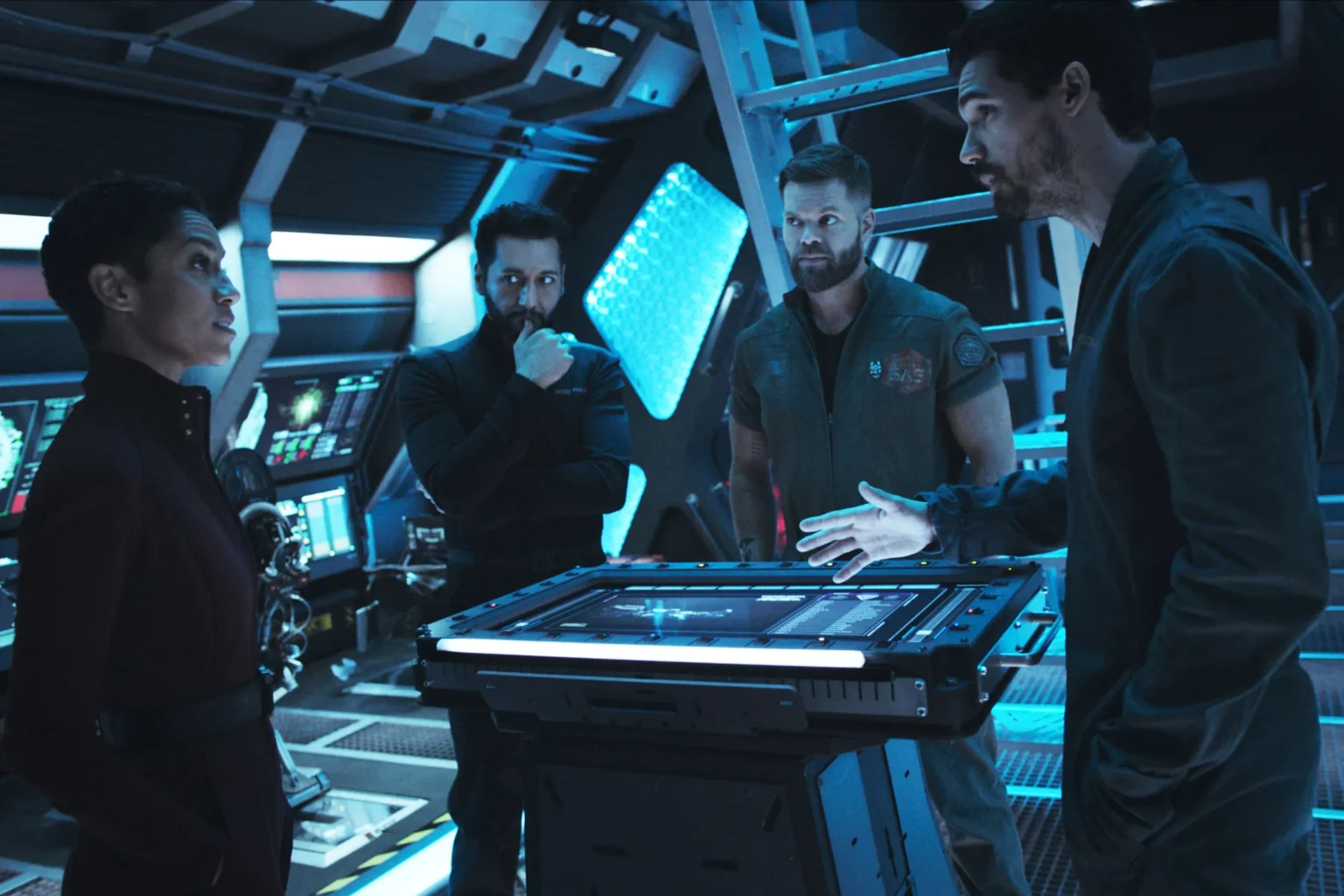 Les membres d'un vaisseau spatiales sont réunis autour d'une table et semblent contrariés.