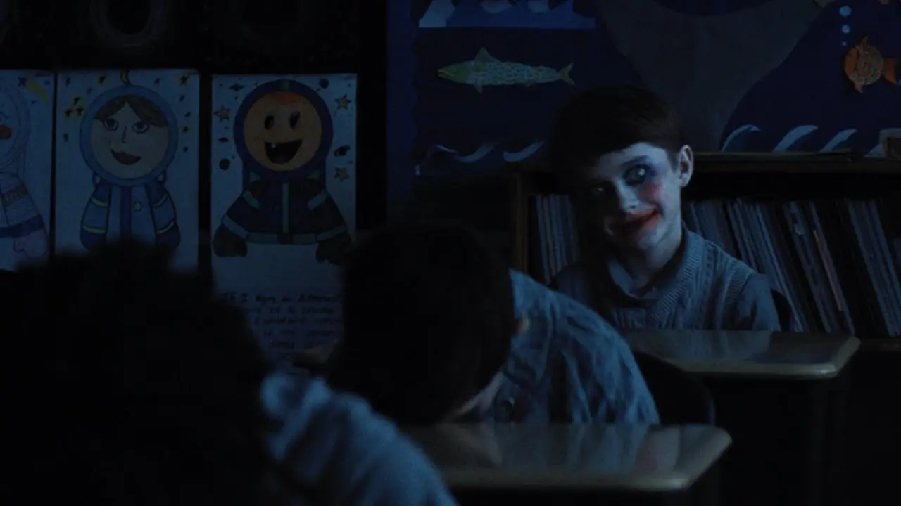 Une salle de classe la nuit, tous les enfants sont pourtant la et ont la tête collé sur leur bureau. Un seul à la tête levée et regarde devant lui, il porte un maquillage de clown, l'image est terrifiante.