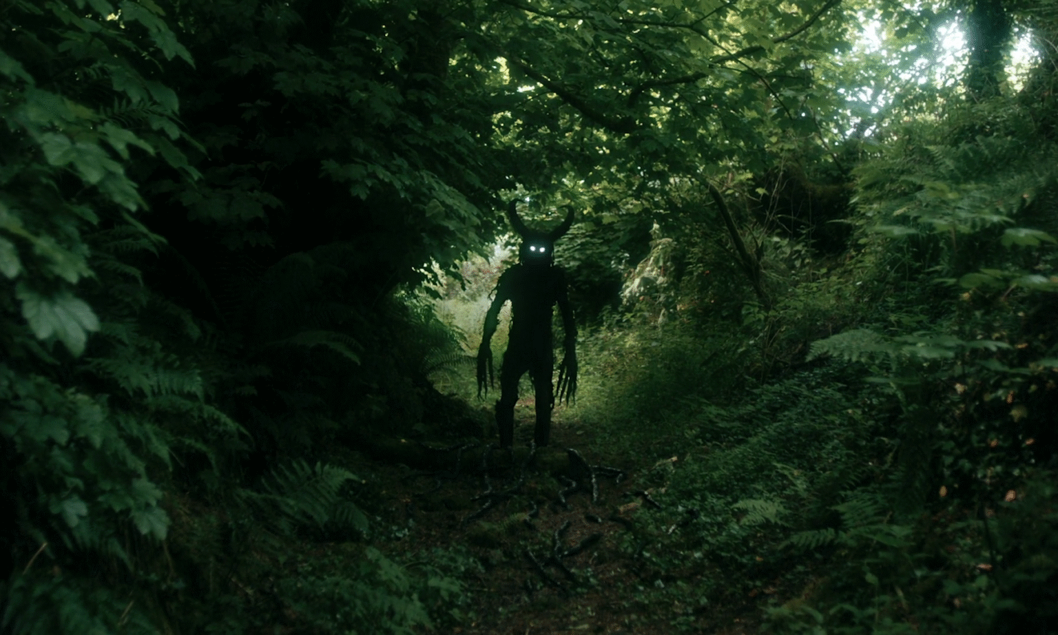 Une créature cornue et noire, au centre d'un chemin dans une forêt. Image tirée du film The Severed Sun.