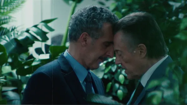 Deux hommes reposent amoureusement leur tête l'un sur l'autre dans un environnement végétal. la scène est tirée de la série Severance.