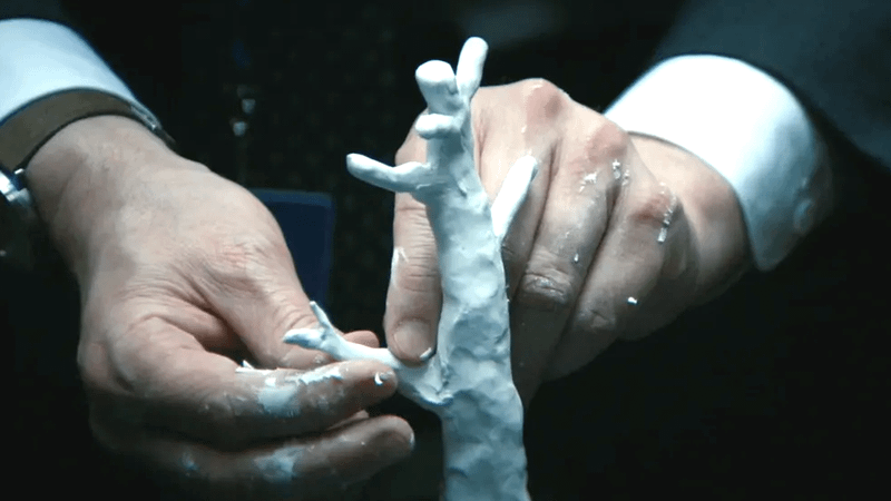 Une homme en costume construit un arbre en argile. la scène est tirée de la série Severance.