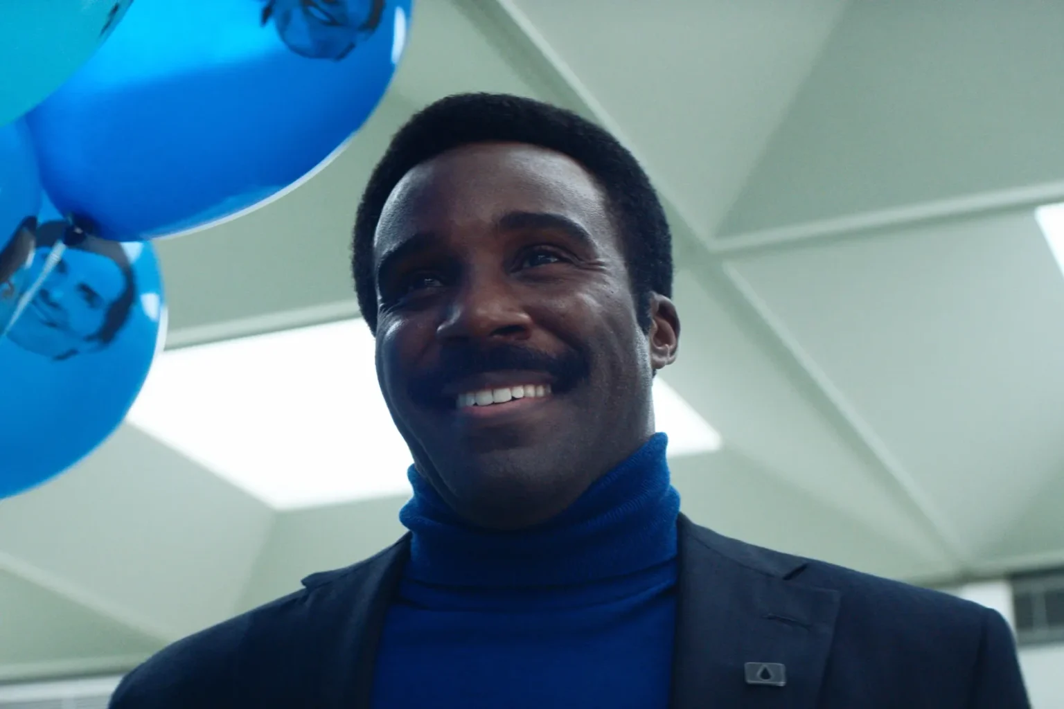 Mr. Milkshike de la série Severance, portée des ballons bleus avec un sourire malsaint.