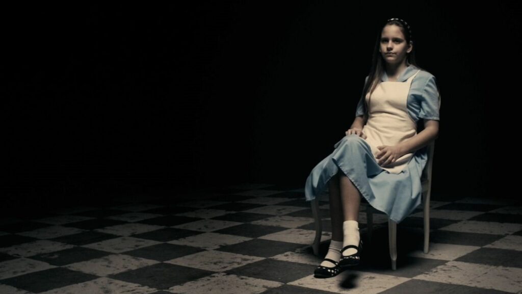 Une femme, en tenue de la jeune fille à la perle, de Vermeer, assise sur une chaise dans une pièce sombre. L'image est tirée du film A Serbian Film