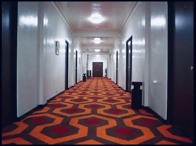 Un couloir d'hôtel aux motifs rouge et orange, un peu psychédélique. Image tirée du film Shining de Kubrick