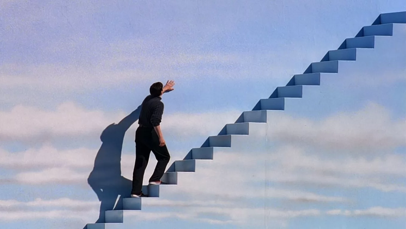 Un homme monte un escalier qui semble être dans le ciel. L'image est tiré du film Truman Show.