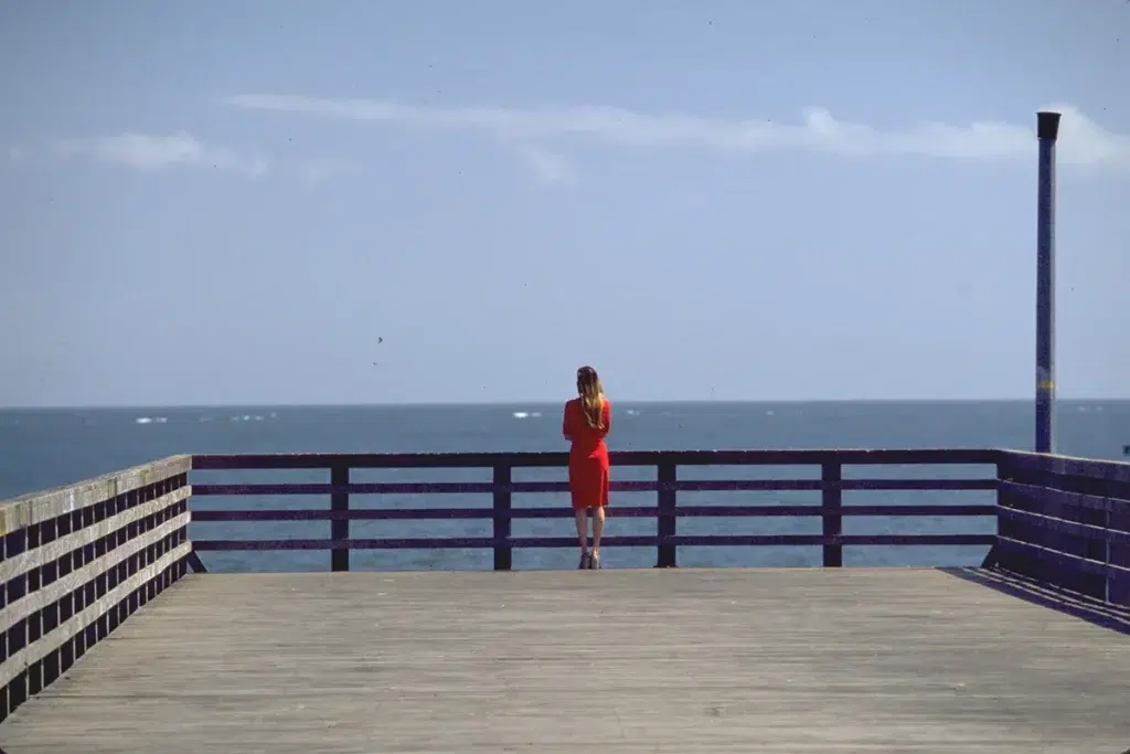 Une femme en robe rouge attend seul au bon d'un belvédère. La lumière du jour est très forte. l'image est tirée du film Requiem for a dream